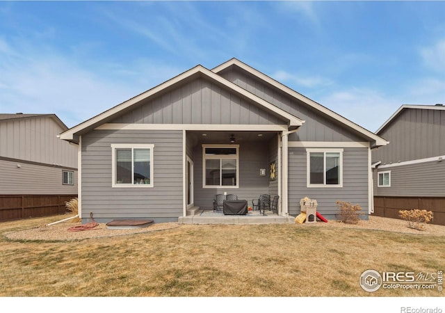 rear view of house featuring board and batten siding, a patio area, a yard, and fence