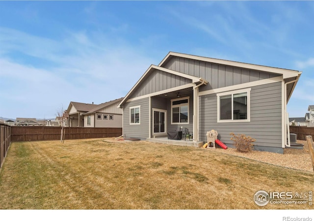 rear view of property featuring board and batten siding, a fenced backyard, a yard, and a patio