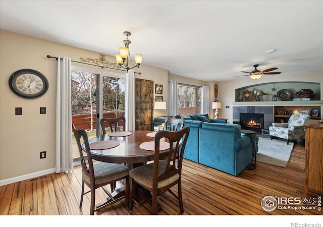 dining room featuring baseboards, visible vents, a tiled fireplace, wood finished floors, and ceiling fan with notable chandelier