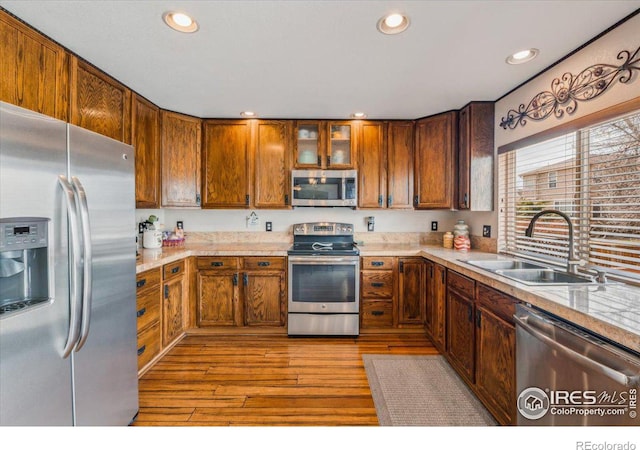 kitchen featuring stainless steel appliances, recessed lighting, glass insert cabinets, a sink, and light wood-type flooring