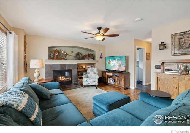 living area with ceiling fan, baseboards, a tiled fireplace, and wood finished floors