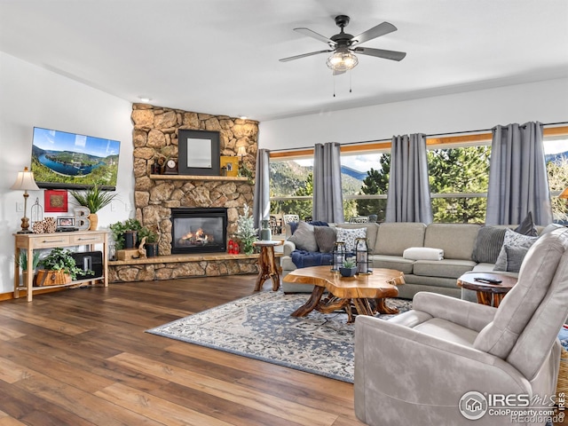 living area featuring a ceiling fan, wood finished floors, and a stone fireplace