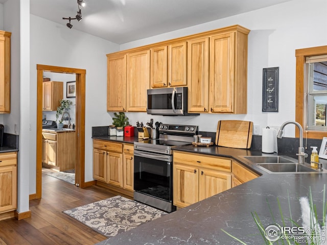 kitchen featuring baseboards, dark wood-style floors, appliances with stainless steel finishes, a sink, and track lighting