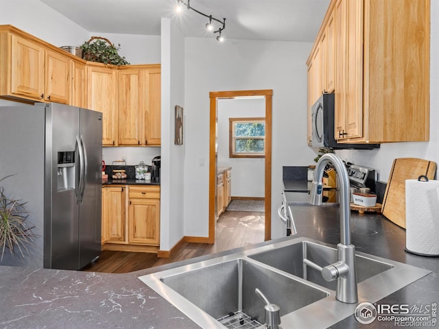 kitchen featuring dark countertops, dark wood-style floors, appliances with stainless steel finishes, light brown cabinets, and a sink