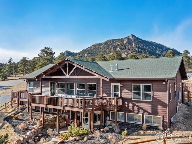 view of front of home with a deck with mountain view, roof with shingles, and a patio