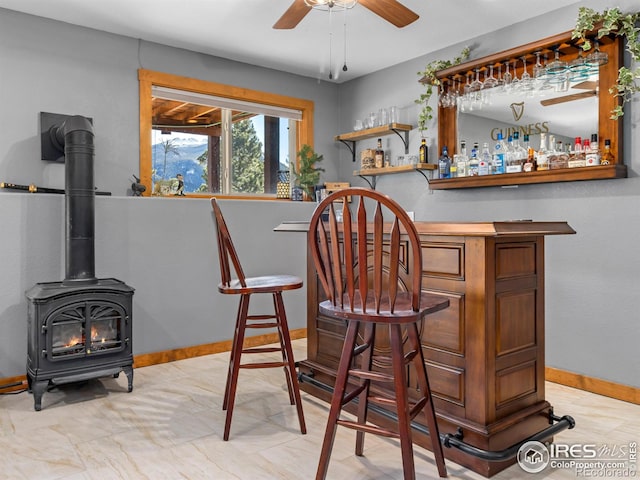 bar with a bar, a wood stove, baseboards, and a ceiling fan