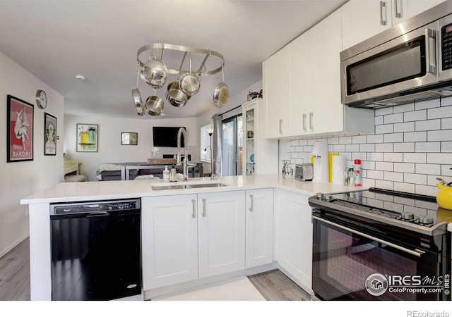 kitchen with white cabinets, open floor plan, a peninsula, black appliances, and a sink