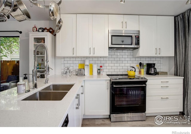 kitchen featuring tasteful backsplash, stainless steel microwave, white cabinets, a sink, and black range with electric cooktop