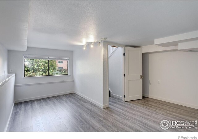 empty room with a textured ceiling, wood finished floors, and baseboards