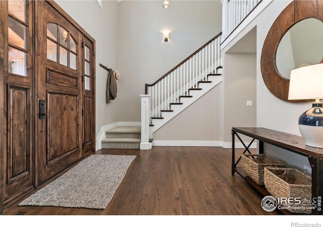 foyer entrance featuring dark wood-type flooring, stairway, a high ceiling, and baseboards