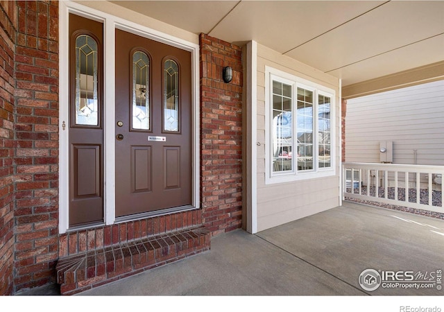 view of exterior entry featuring covered porch and brick siding