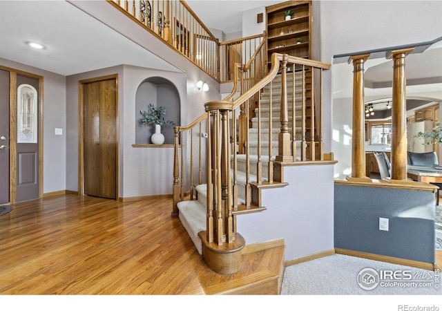 foyer featuring decorative columns, stairs, baseboards, and wood finished floors