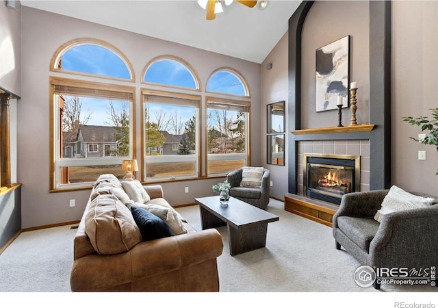 living area with carpet floors, ceiling fan, high vaulted ceiling, a tile fireplace, and baseboards