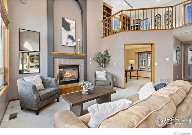 living area featuring a tiled fireplace, a high ceiling, carpet, and visible vents