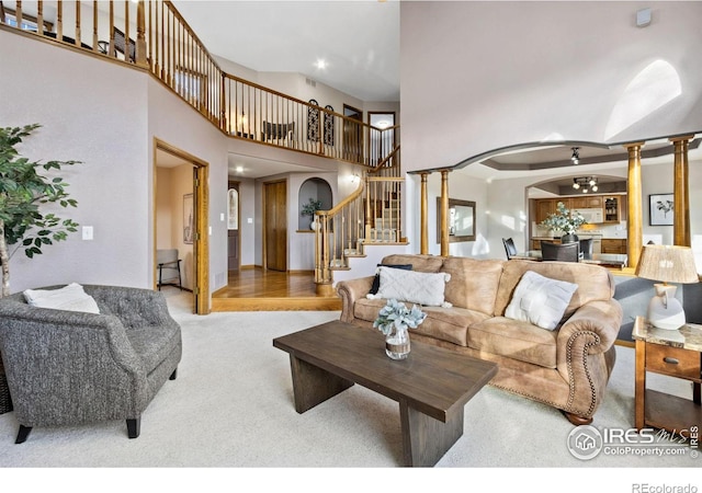 carpeted living room with arched walkways, a high ceiling, stairway, and ornate columns