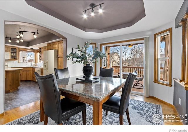 dining room featuring light wood-type flooring, a raised ceiling, arched walkways, and baseboards