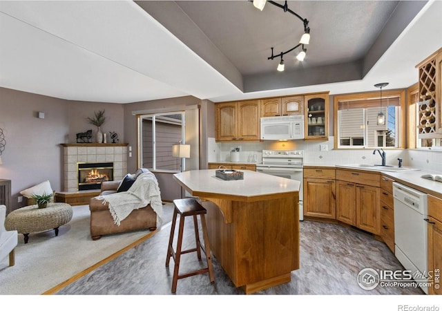 kitchen with a tray ceiling, a tiled fireplace, glass insert cabinets, a sink, and white appliances