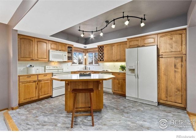 kitchen with white appliances, a kitchen island, a tray ceiling, light countertops, and a sink