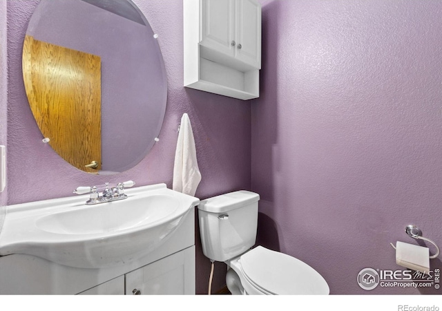 half bathroom featuring toilet, vanity, and a textured wall