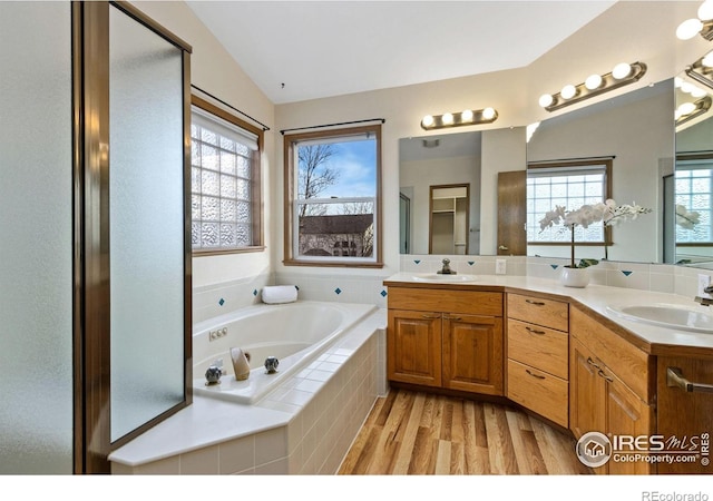 bathroom with lofted ceiling, a garden tub, a sink, and wood finished floors