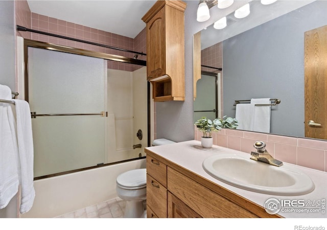 bathroom with combined bath / shower with glass door, vanity, toilet, and tasteful backsplash