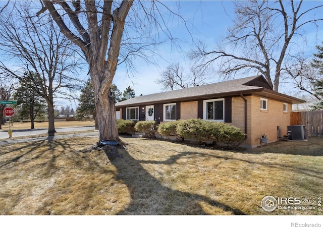 ranch-style house featuring brick siding, a front lawn, central AC unit, and fence