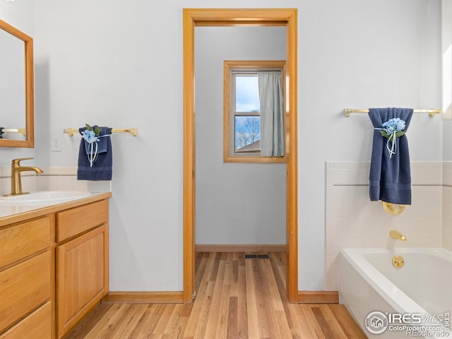 full bathroom featuring visible vents, vanity, a bath, and wood finished floors