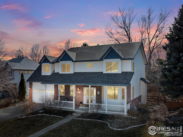 traditional home with a garage, driveway, roof with shingles, covered porch, and brick siding