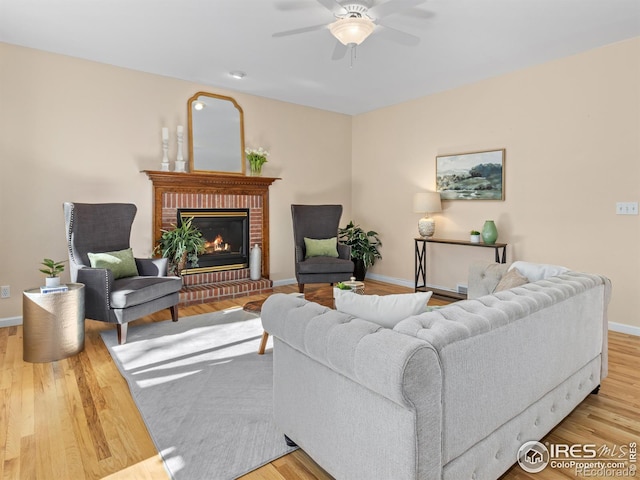 living room featuring a brick fireplace, wood finished floors, a ceiling fan, and baseboards