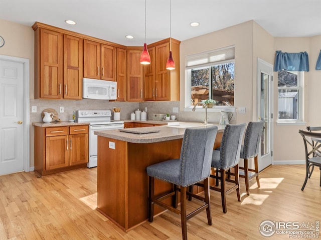 kitchen featuring a breakfast bar, brown cabinets, light wood-style flooring, backsplash, and white appliances