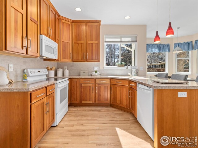 kitchen featuring white appliances, light wood finished floors, brown cabinetry, a peninsula, and backsplash