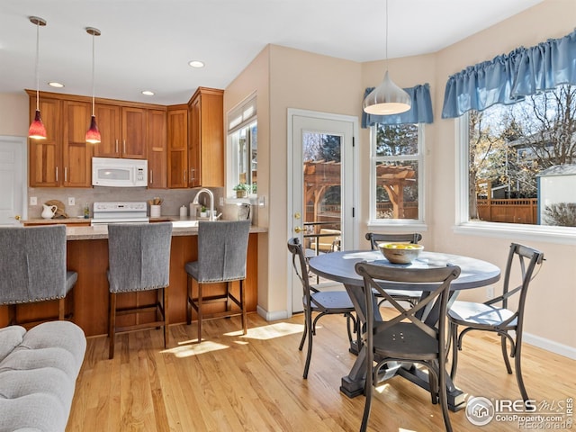 kitchen with white appliances, decorative backsplash, brown cabinetry, light wood-style flooring, and hanging light fixtures