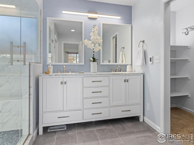 full bath with a sink, double vanity, a marble finish shower, and baseboards