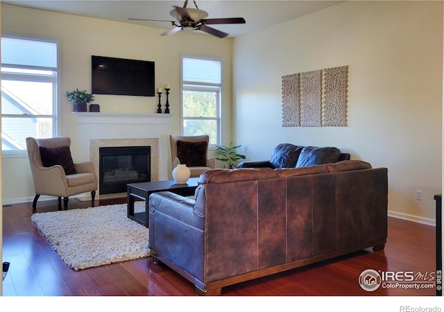 living room with a glass covered fireplace, dark wood-style floors, baseboards, and ceiling fan