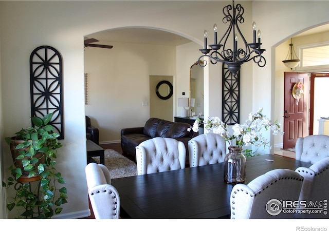 dining space with ceiling fan with notable chandelier, baseboards, and wood finished floors