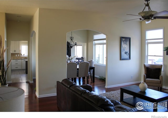 living room featuring ceiling fan with notable chandelier, wood finished floors, arched walkways, and baseboards