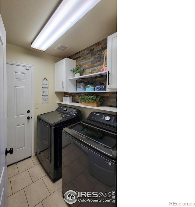 clothes washing area with visible vents, cabinet space, washing machine and dryer, and light tile patterned flooring