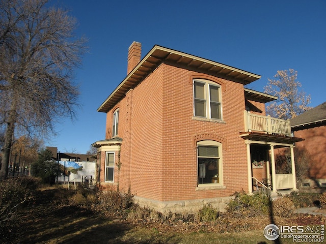 view of side of home featuring brick siding, a chimney, and a balcony