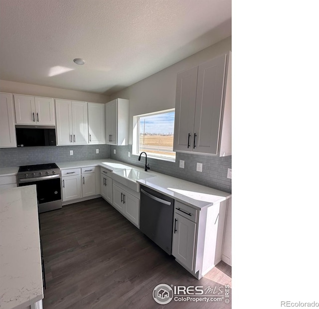 kitchen featuring stainless steel appliances, dark wood-style flooring, white cabinetry, and light stone counters