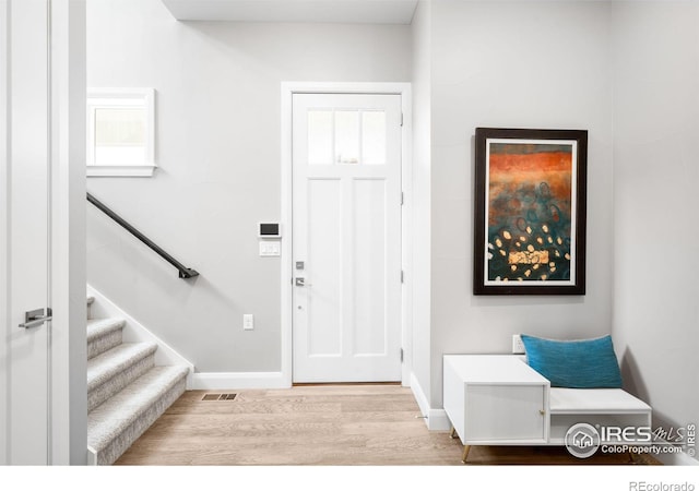 entryway with stairs, visible vents, baseboards, and wood finished floors