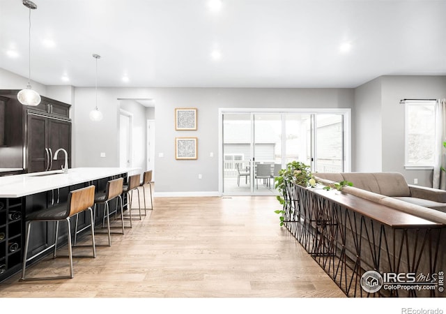 kitchen featuring light wood finished floors, light countertops, a sink, a kitchen breakfast bar, and baseboards