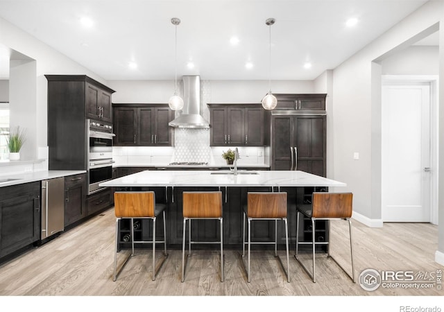 kitchen featuring wall chimney exhaust hood, a sink, stainless steel appliances, light wood-type flooring, and backsplash