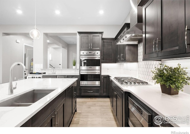 kitchen with tasteful backsplash, wall chimney exhaust hood, decorative light fixtures, stainless steel appliances, and a sink