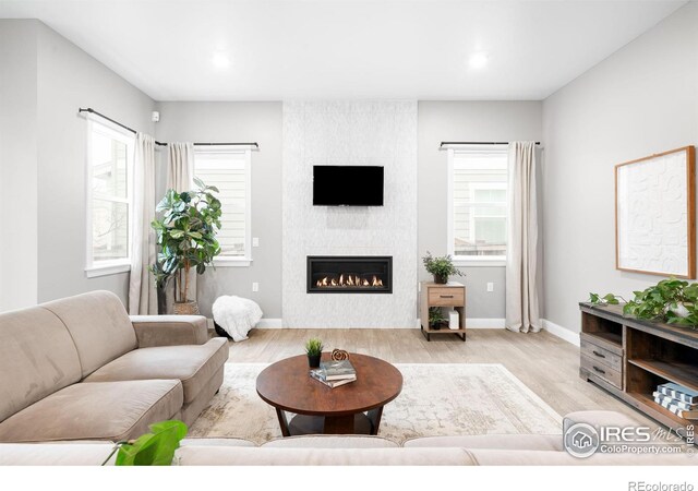 living room with light wood-type flooring, a large fireplace, baseboards, and recessed lighting