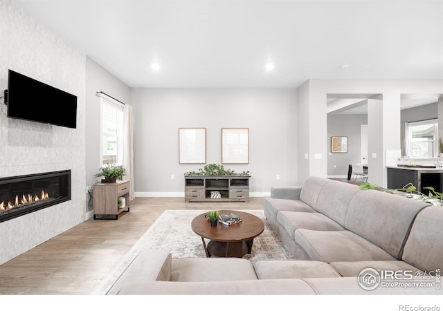 living room featuring light wood finished floors, a tiled fireplace, a wealth of natural light, and baseboards