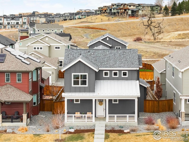 view of front of property with covered porch, fence, roof with shingles, a residential view, and board and batten siding