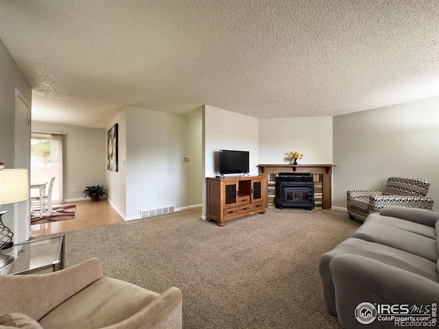 carpeted living room with a glass covered fireplace, visible vents, a textured ceiling, and baseboards