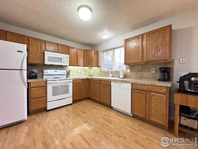 kitchen featuring light wood finished floors, backsplash, brown cabinetry, a sink, and white appliances