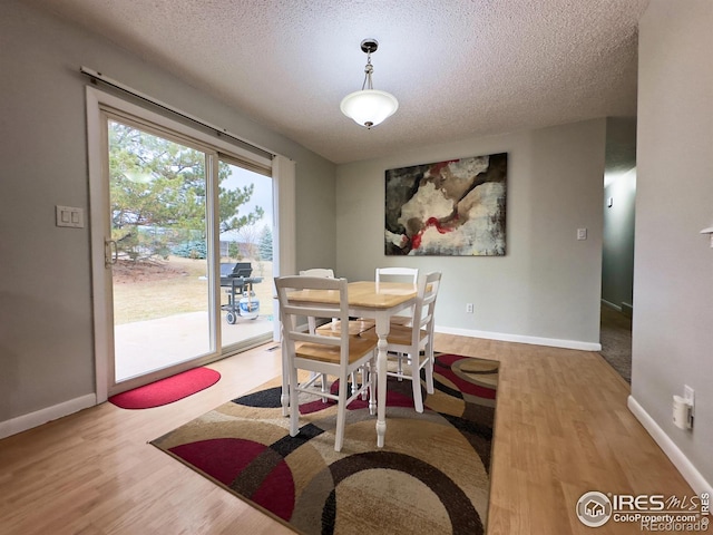 dining space featuring a textured ceiling, wood finished floors, and baseboards