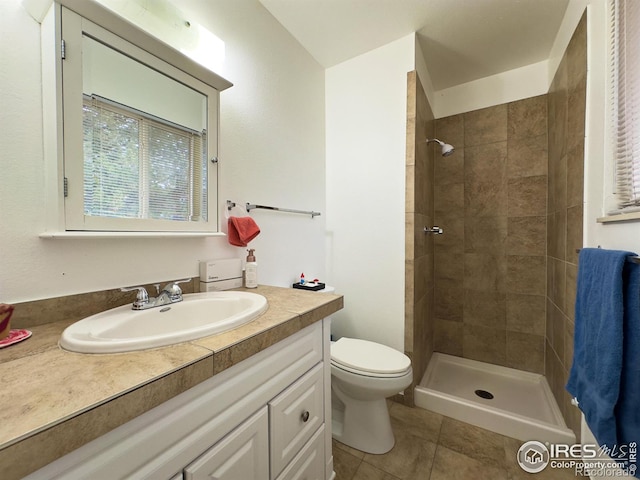 bathroom featuring toilet, tile patterned flooring, tiled shower, and vanity